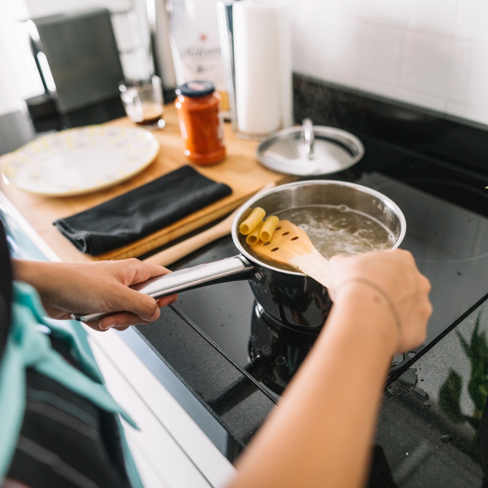 a woman boiling rigatoni pasta on electric stove